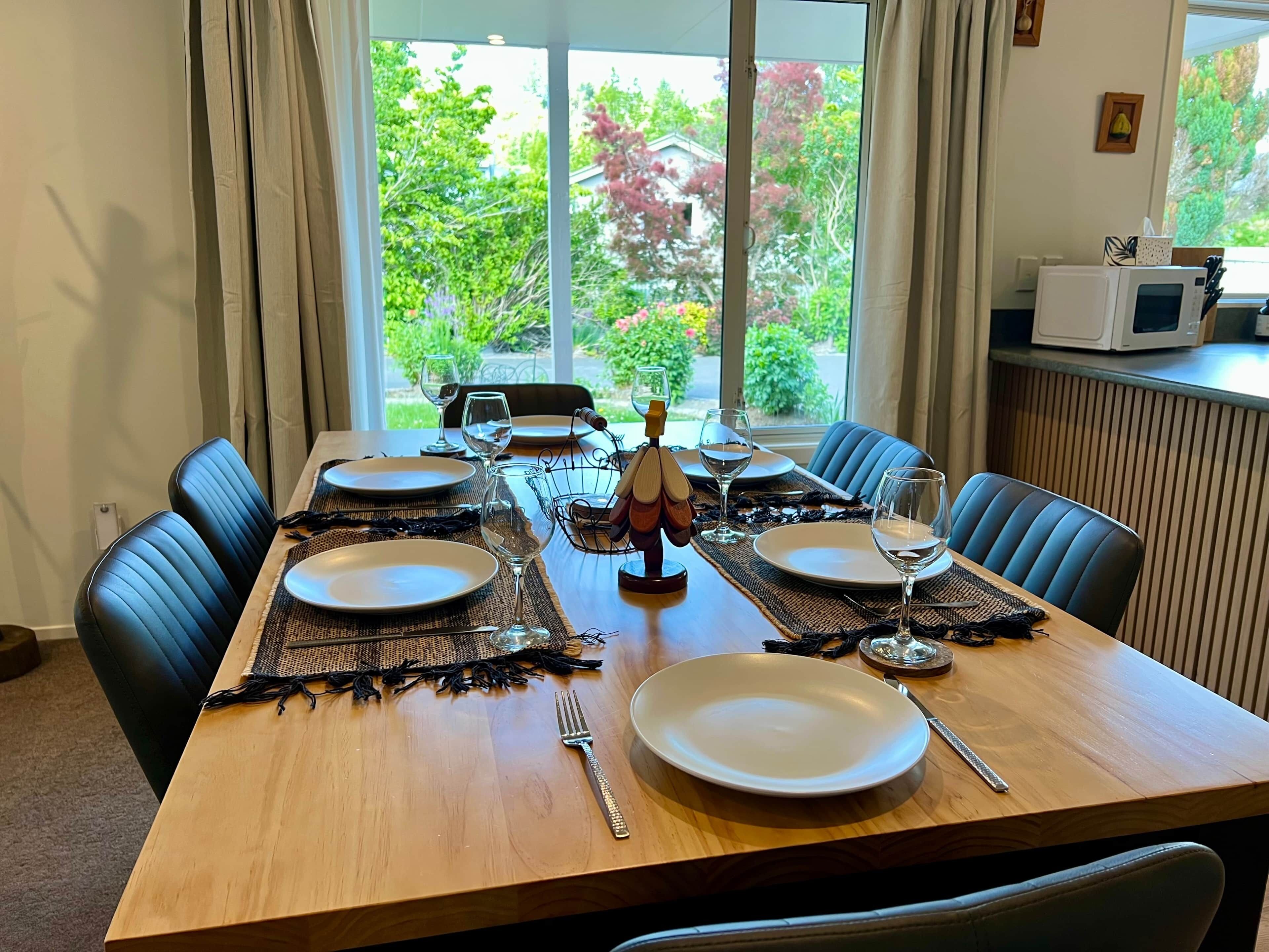 Une table à manger dressée avec des assiettes, des verres et des couverts, donnant sur un paysage verdoyant.
