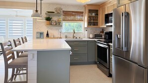 A modern kitchen with a central island, stainless steel appliances, and wooden cabinets. - Coastal Chic 2BR – Modern Stay Near Manasota Key (Englewood)