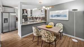 A modern kitchen with a central island, a dining area with floral chairs, and a large framed picture on the wall.