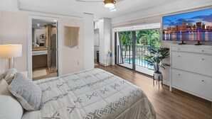 A bedroom with a bed, a ceiling fan, a TV, and a view of a cityscape through a sliding door.