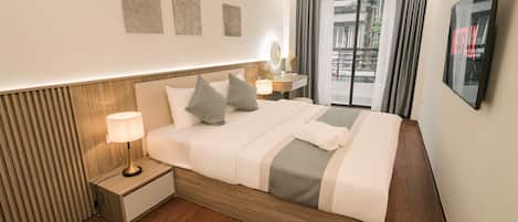 A hotel room with a bed, bedside lamp, a small table with a mirror, a TV, and a window with curtains.