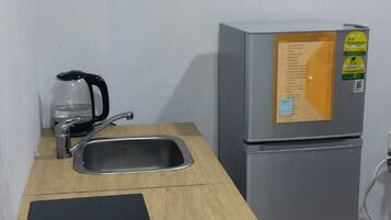 Una kitchenette pequeña con un lavamanos, una tetera, un refrigerador y un calentador portátil sobre una encimera de madera.