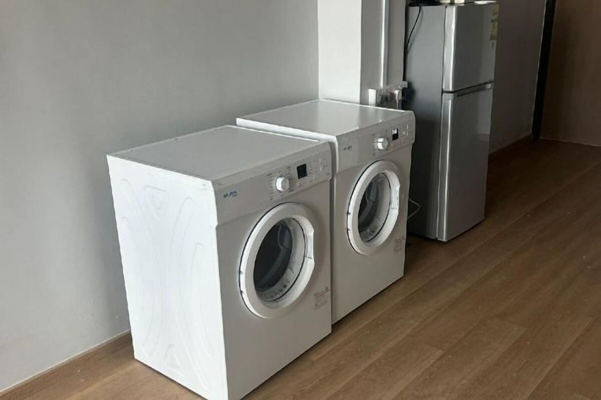 A compact laundry area with a front-loading washer and dryer, a refrigerator, and a wooden floor.