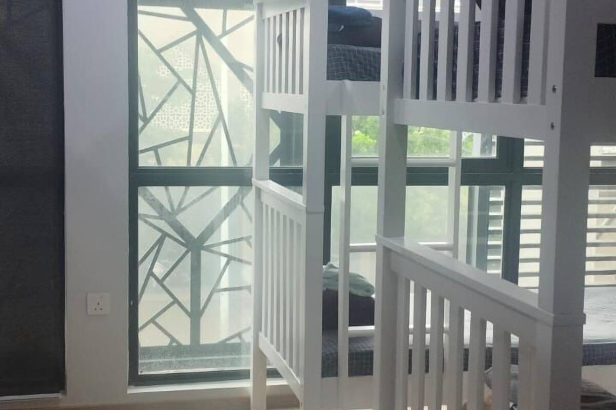 Una habitación con piso de madera, barandillas blancas y vista a través de una ventana con diseño geométrico.