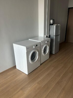A laundry area with a washing machine and dryer, a small refrigerator, and a wooden floor.