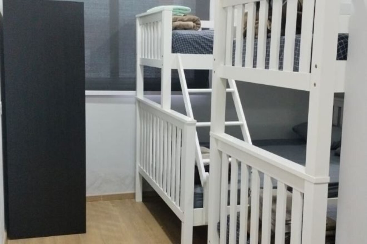 Een kamer met twee witte stapelbedden, een raam en een deur.