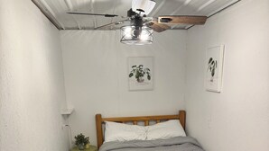 Un dormitorio pequeño y acogedor con una cama de madera, un ventilador de techo y dos cuadros en la pared.