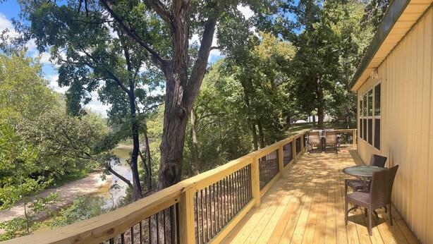 Una terraza de madera con barandilla que da a un río, rodeada de árboles.