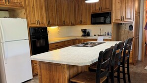 Una cocina con armarios de madera, un refrigerador blanco, una estufa negra y una isla grande con taburetes de bar.