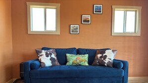 A blue sofa with cowhide pillows, a leather rug, and framed pictures on a wall. - Private Cabin Near Big Bend National Park (Alpine)