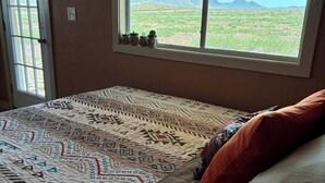 A bedroom with a bed, a window with a view of mountains, and a door. - Private Cabin Near Big Bend National Park (Alpine)