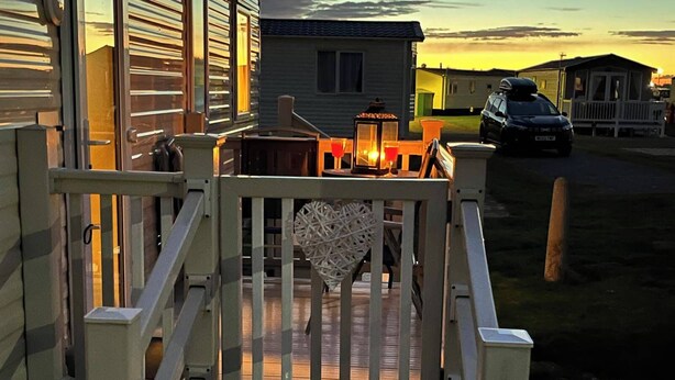 Ingresso recintato di una casa mobile con veranda in legno e decorazione a forma di cuore.