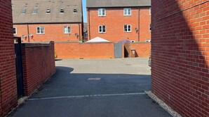 A parking area with a paved surface, surrounded by red brick buildings with multiple windows and satellite dishes. - Derby Luxury Apartment - Foss Road- Sleeps4 (Derby)