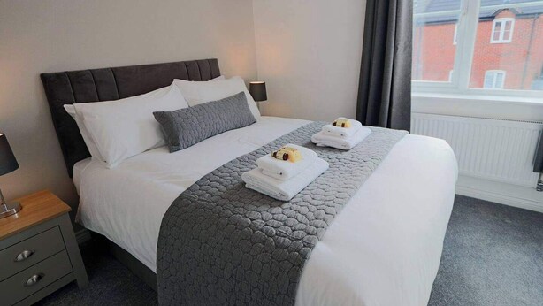 A neatly made bed with a grey quilt, white pillows, and two towels on the bed. - Derby Luxury Apartment - Foss Road- Sleeps4 (Derby)