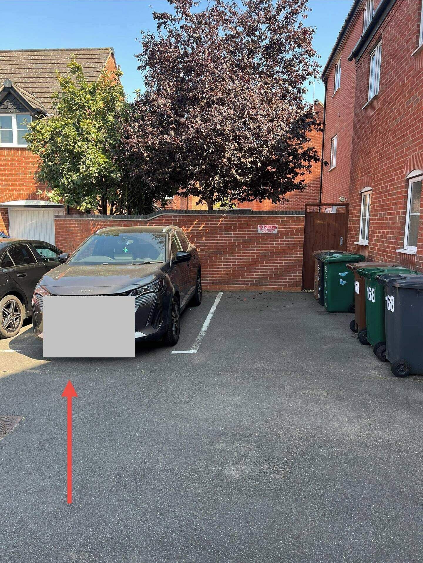 En parkeringsplats med en bil, en skylt med texten ”Parkering förbjuden” och gröna soptunnor.