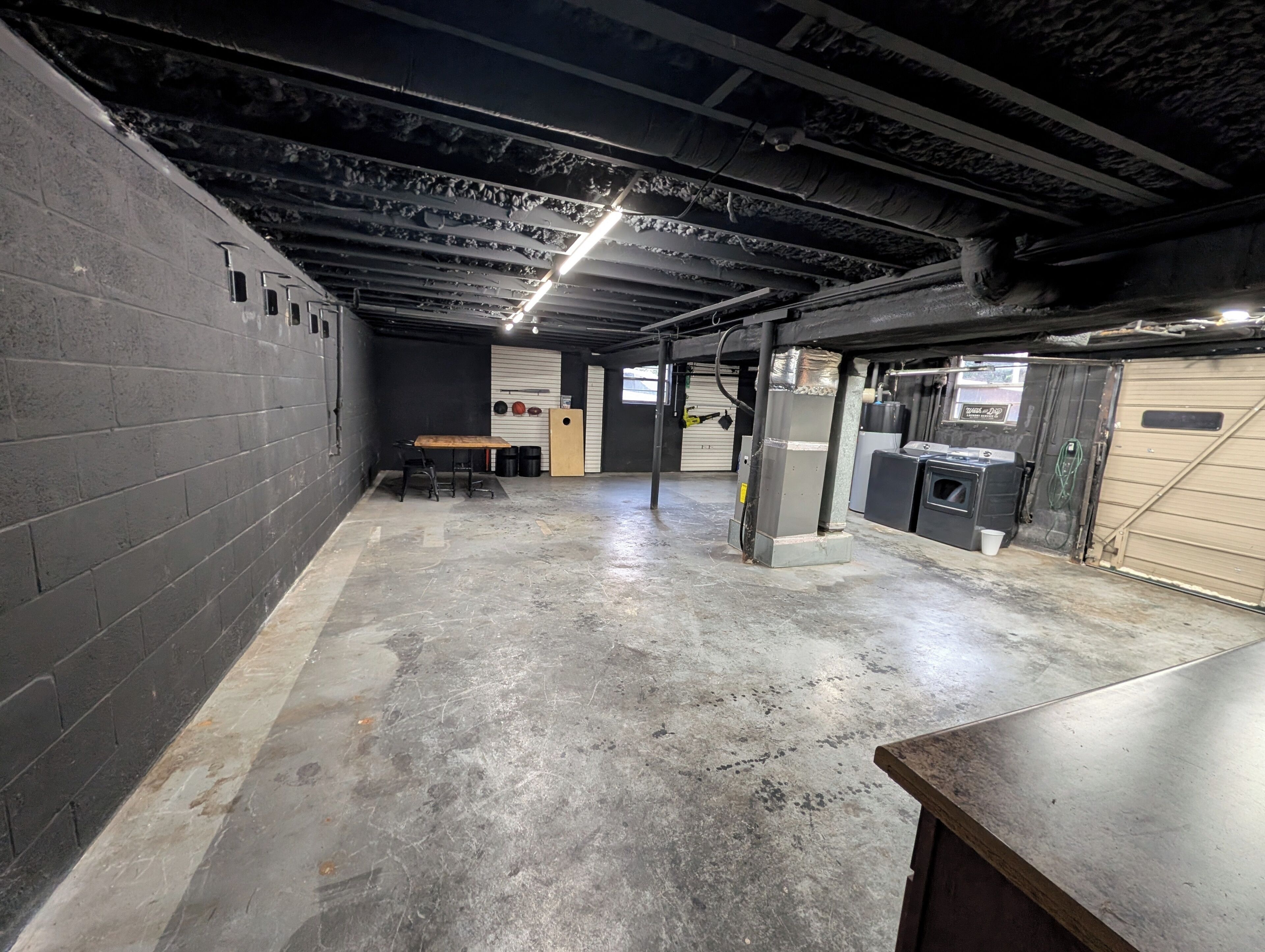 A spacious, industrial-style basement with concrete floors and walls, a table with chairs, and a water heater.
