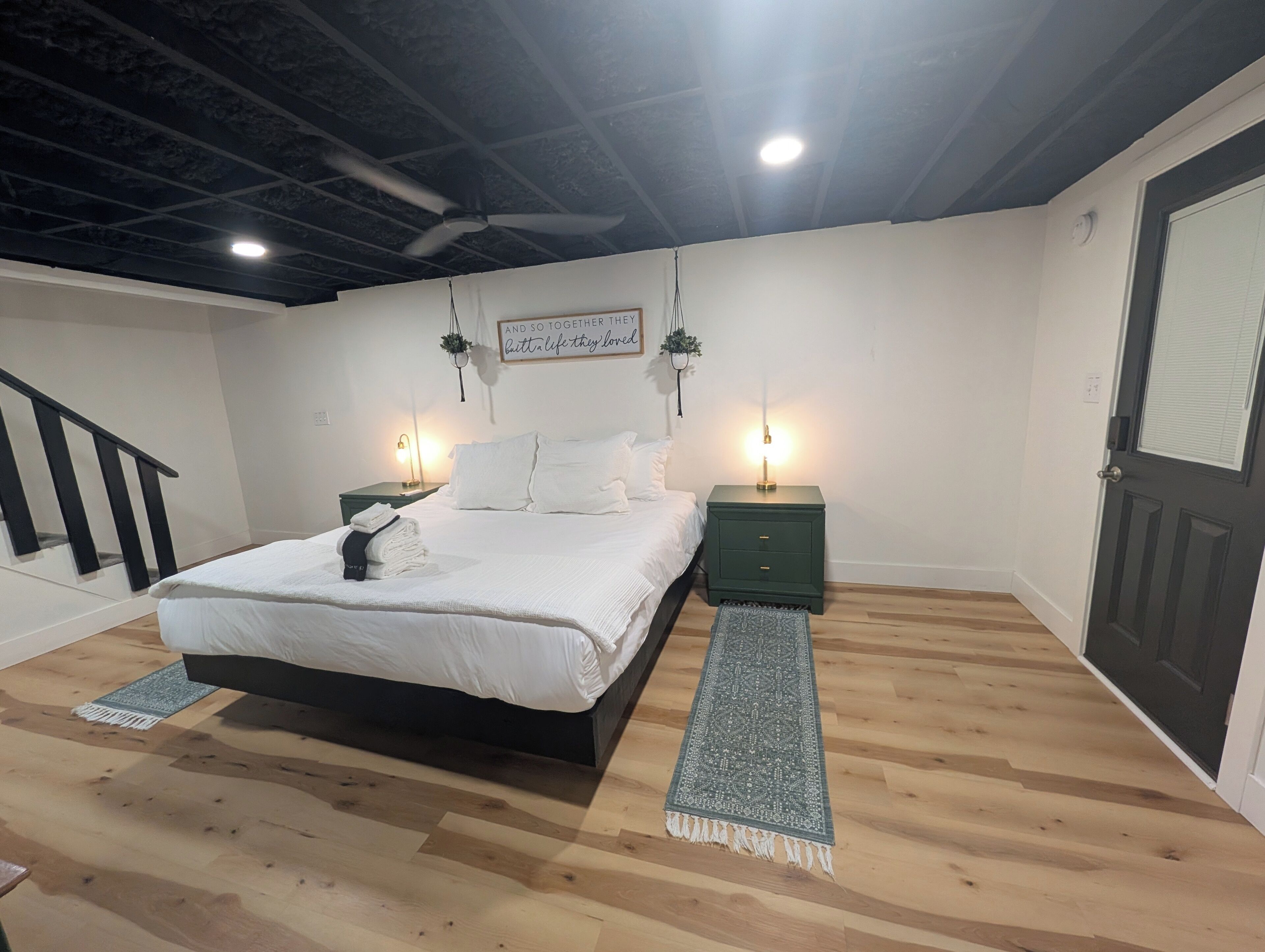 A bedroom with a bed, two bedside tables, a ceiling fan, a wall-mounted sign, and a door.