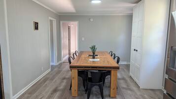 A dining area with a wooden table and black chairs, a small plant on the table, and a white door in the background.