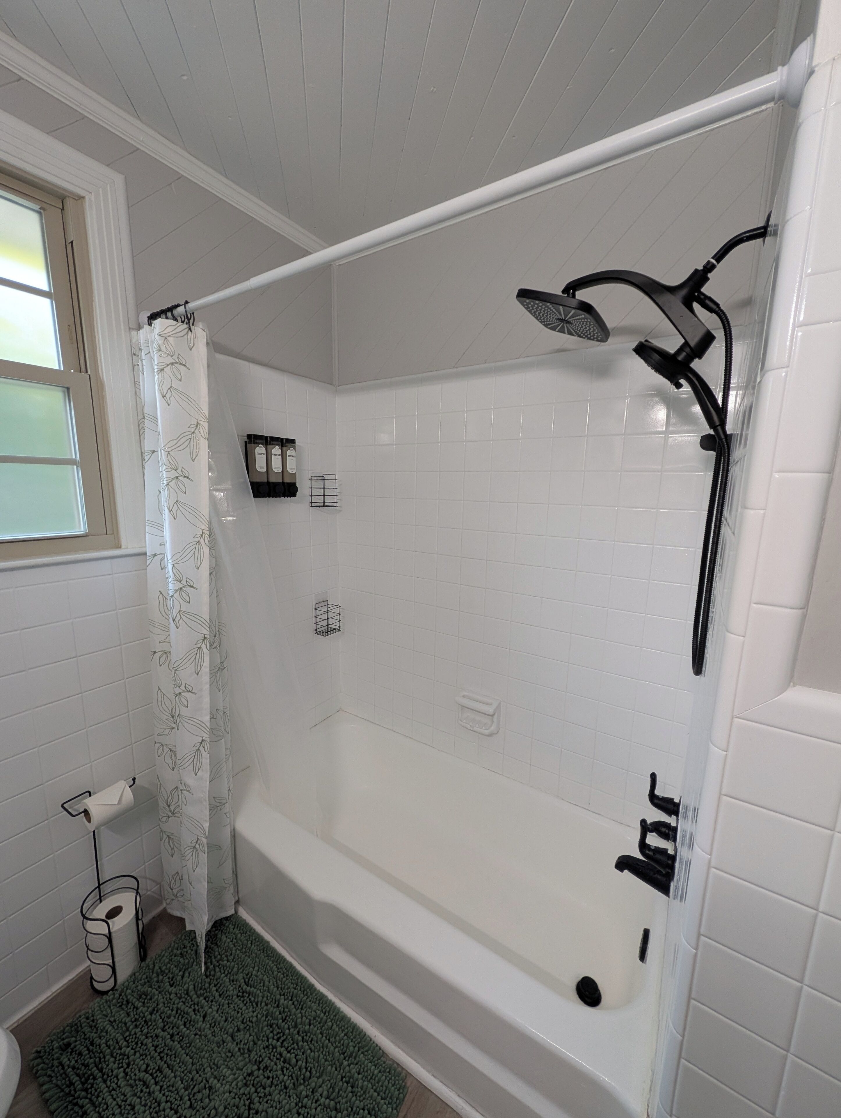 A bathroom with a bathtub, shower, toilet, and a window with a curtain.