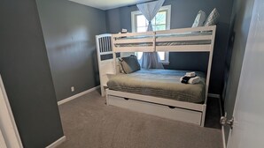 Een slaapkamer met een stapelbed, een plafondventilator, een raam met gordijnen en een vloerbedekking.