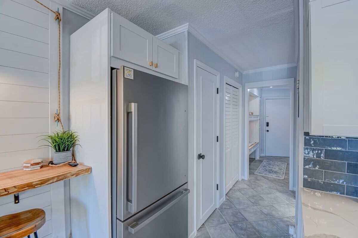 A modern kitchen with white cabinetry, a stainless steel refrigerator, and a wooden countertop with a plant.