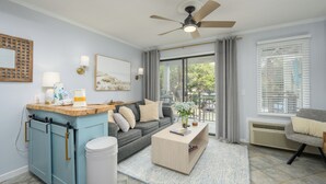 A modern living room with a grey sofa, a wooden coffee table, and a ceiling fan. - Beachfront Escape w Balcony+Pool (Hilton Head Island)