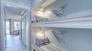 A hallway with a bench, a wall with a whale mural, and a door leading to another room. - Beachfront Escape w Balcony+Pool (Hilton Head Island)