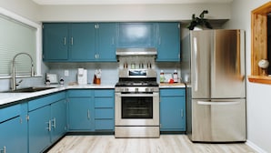 Una cocina con armarios verde azulado, electrodomésticos de acero inoxidable y piso de madera.