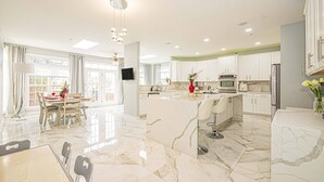 A modern kitchen with white cabinets, a marble island, and a dining area with a table and chairs.