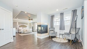 A spacious living room with hardwood flooring, a fireplace, a ceiling fan, and a seating area with a chair and a couch.