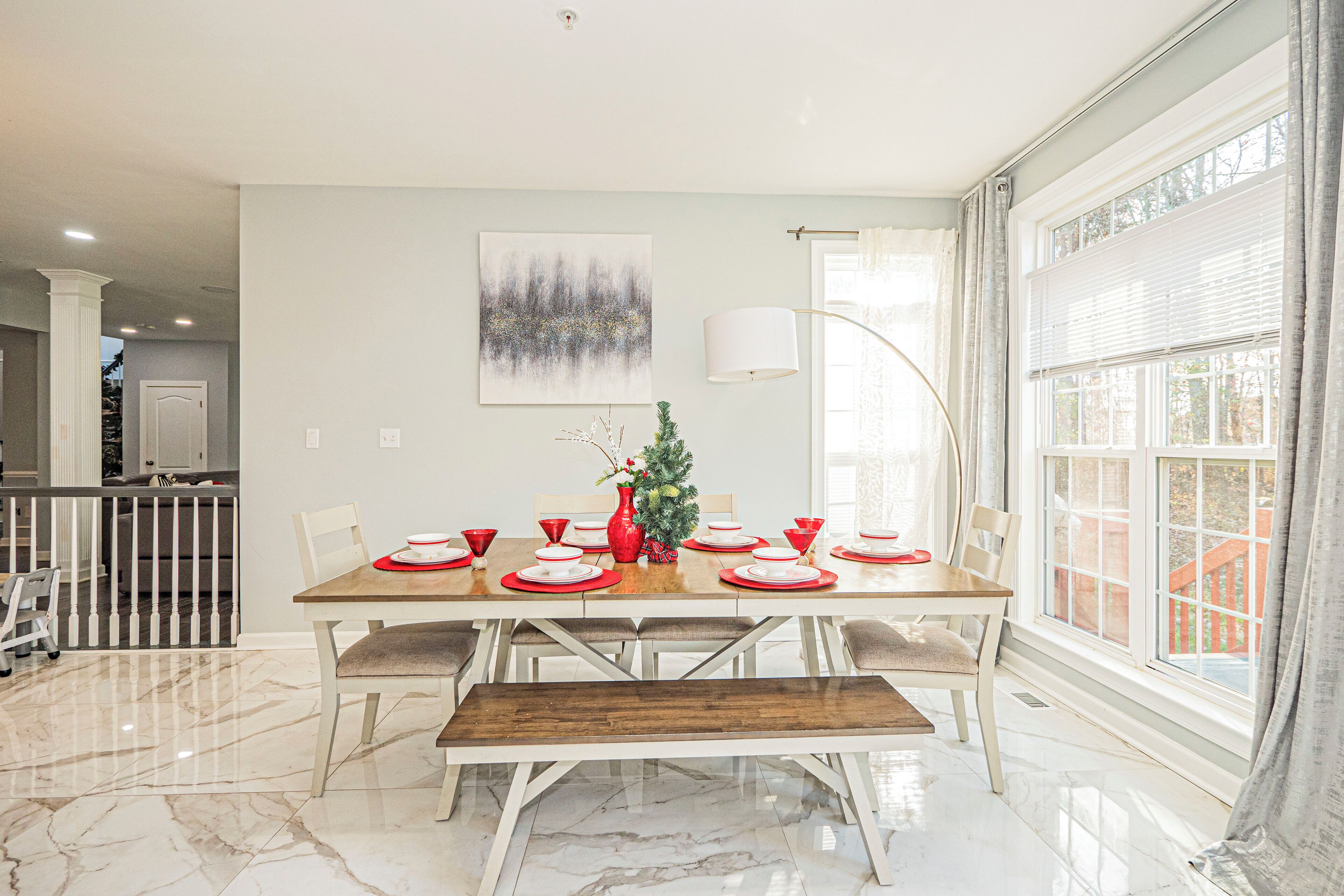 A dining area with a marble floor, a wooden bench, and a table set for six with red and white plates.