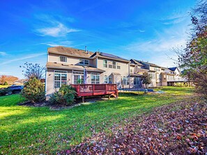 A two-story residential house with a red deck, a covered porch, and a well-maintained lawn.