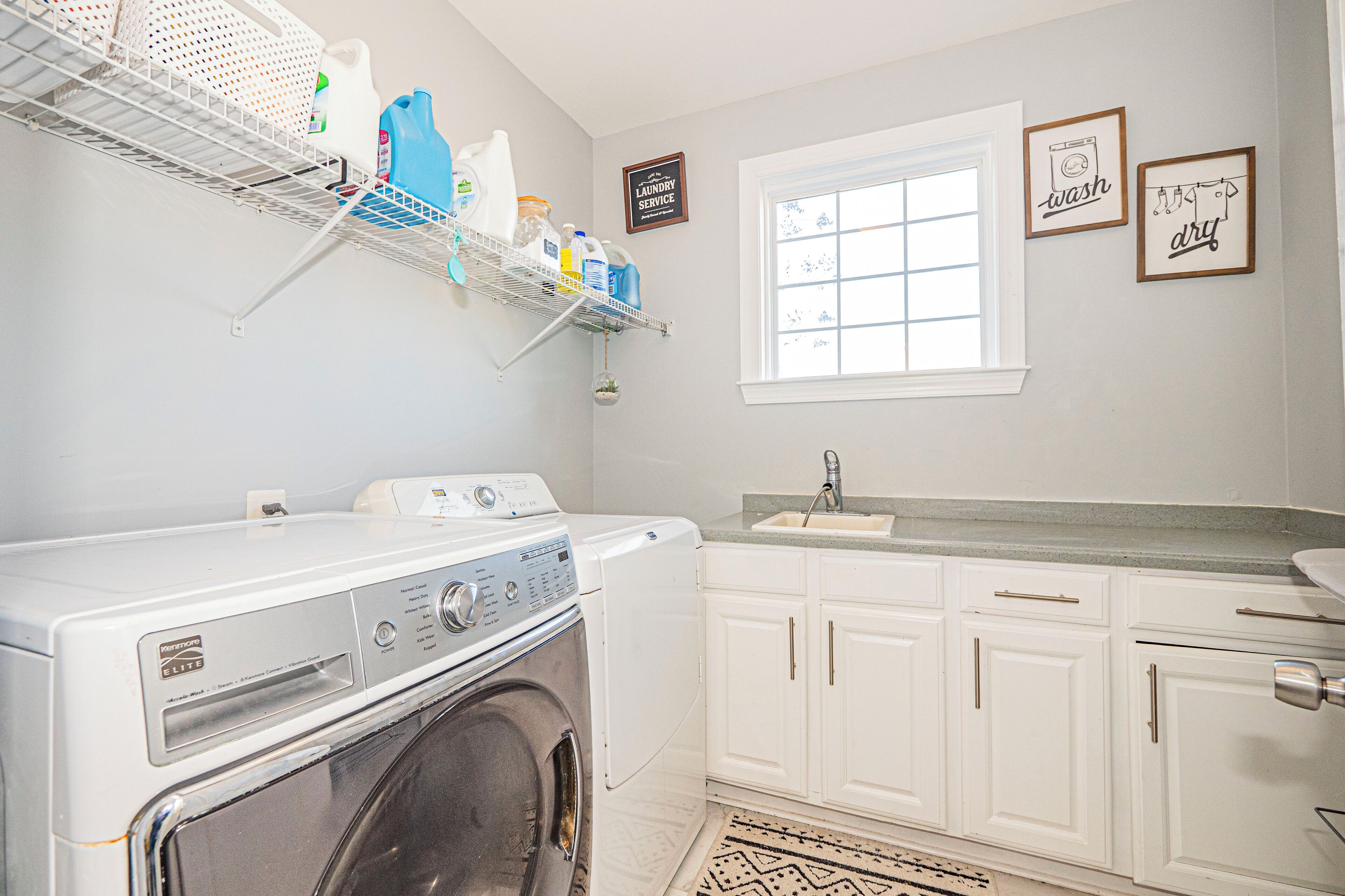A laundry room with a washing machine, a shelf with cleaning supplies, a window, and a sink.