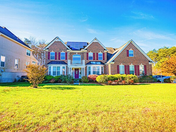 A large brick house with a front porch, solar panels, and a well-maintained lawn.