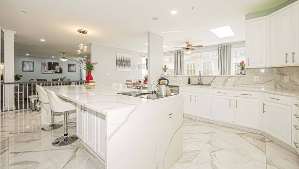 A spacious kitchen with a large island, white cabinetry, and marble flooring.