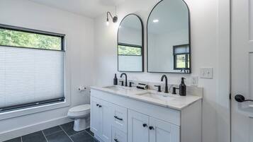 Een moderne badkamer met toilet, twee wasbakken, een spiegel en een raam.
