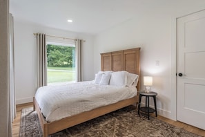 A bedroom with a bed, a bedside table with a lamp, a door, and a window with curtains.