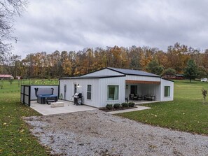 A single-story building with a covered patio, a grill, and a small outdoor seating area.