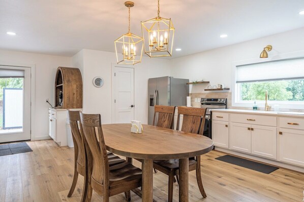 A modern kitchen with a central island, wooden chairs, a round dining table, and pendant lighting.
