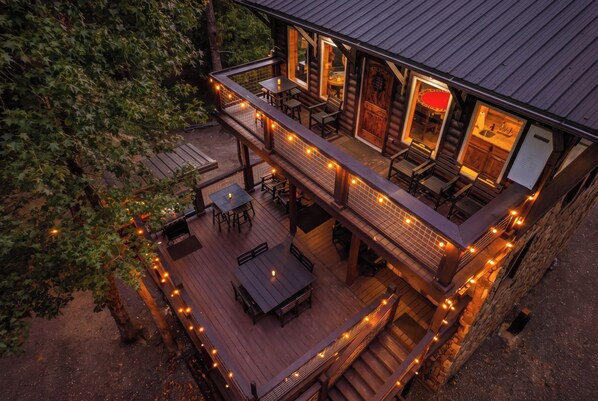 A two-story wooden cabin with a deck, outdoor seating, and string lights.