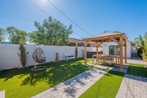 Een achtertuin met een houten pergola, een witte bank en een ventilator.