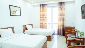 Habitación de hotel con dos camas, un escritorio de madera, una silla y una ventana con cortinas.