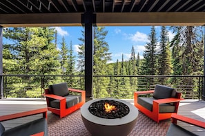 An outdoor deck with a fire pit, two red chairs, and a view of a forest.