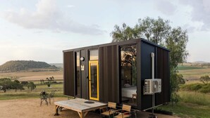 Een moderne, compacte accommodatie met een grote schuifdeur, een klein terras met een tafel en stoelen, en een airconditioning.