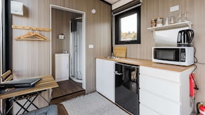 Eine kleine Küche mit Mikrowelle, Spüle und Holzarbeitsplatte. Es gibt einen kleinen Schrank, ein Fenster und ein Regal mit Gläsern und Vorratseinkäufen.