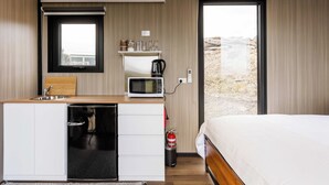 Ein kompaktes Hotelzimmer mit einer Küchenzeile, einem Bett und Blick auf eine verschneite Landschaft.