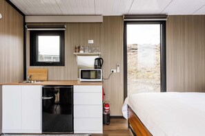A compact hotel room with a kitchenette, a bed, and a view of a snowy landscape. - Melmarie Cosy Retreat X by Tiny Away (Waitati)