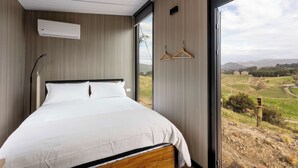 Ein Schlafzimmer mit einem großen Bett, einer Wand-Klimaanlage und Blick auf eine ländliche Landschaft durch ein großes Fenster.
