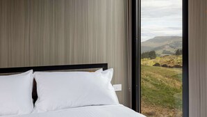 Ein Schlafzimmer mit einem großen Fenster und Blick auf eine hügelige Landschaft.