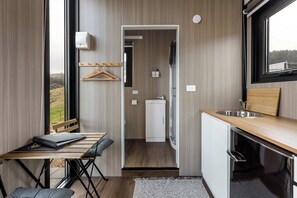 Una kitchenette compacta y moderna con cubierta de madera, un lavamanos y un armario pequeño. Se observa una mesa con una computadora portátil y un perchero.